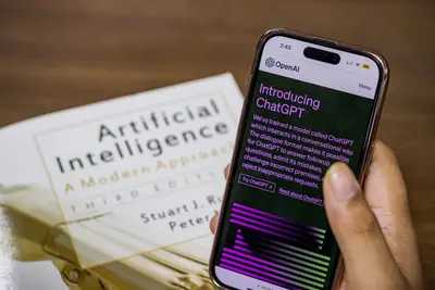 هاتف يعرض تطبيق ChatGPT مجاني بجانب كتاب ذكاء اصطناعي