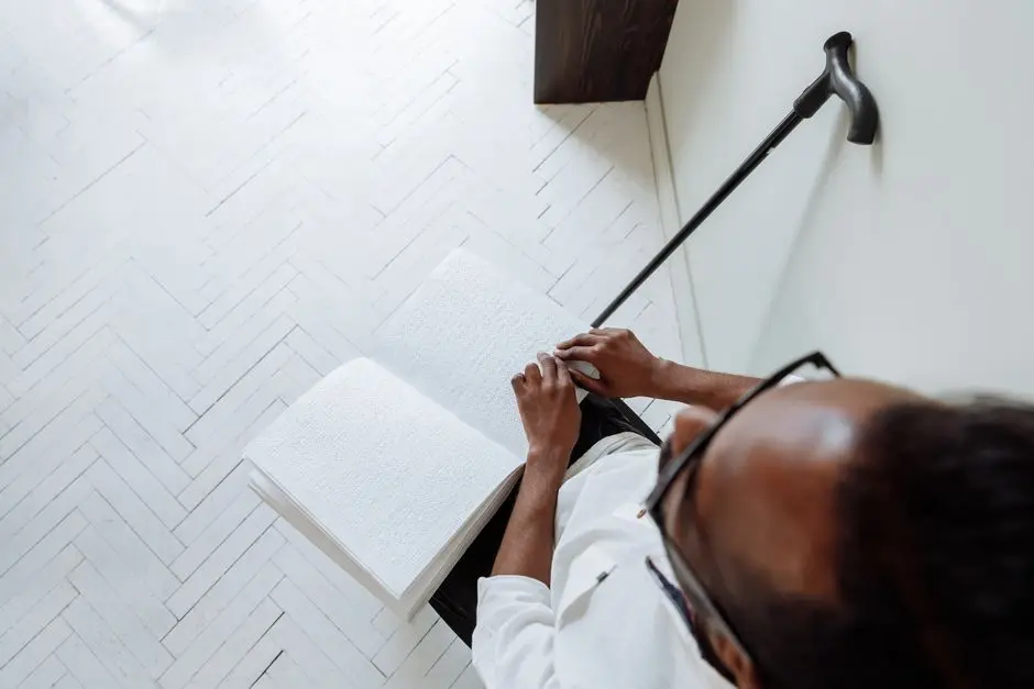 شخص يقرأ كتابًا بطريقة برايل بجانبه عصا بيضاء يمثل تطبيقات الذكاء الاصطناعي للمكفوفين