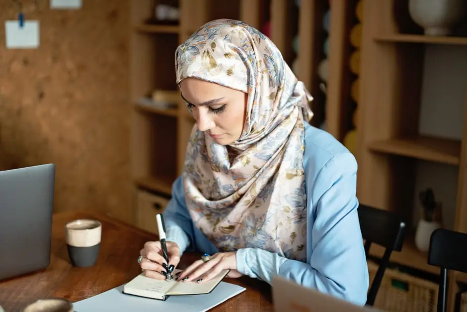 طالبة عربية تستخدم شات جي بي تي للدراسة على اللابتوب مع تدوين الملاحظات